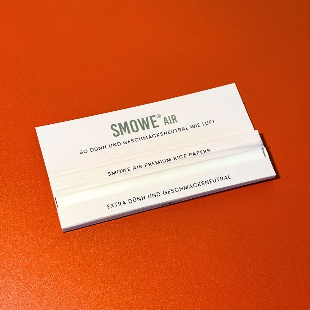 Geöffnete Packung SMOWE AIR Premium Rice Papers Longpapers ohne Filter-Tips auf orangefarbenem Hintergrund.