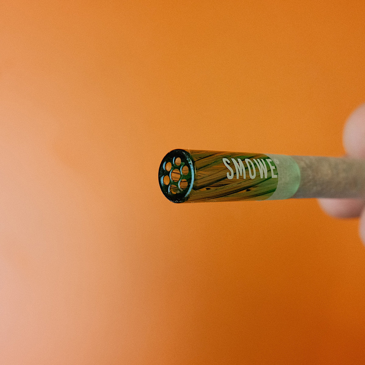 Frontansicht des SMOWE Glasfilters mit Waben-Lochsieb (Flowfilter) und grüner J-Band Banderole auf orangefarbenem Hintergrund.