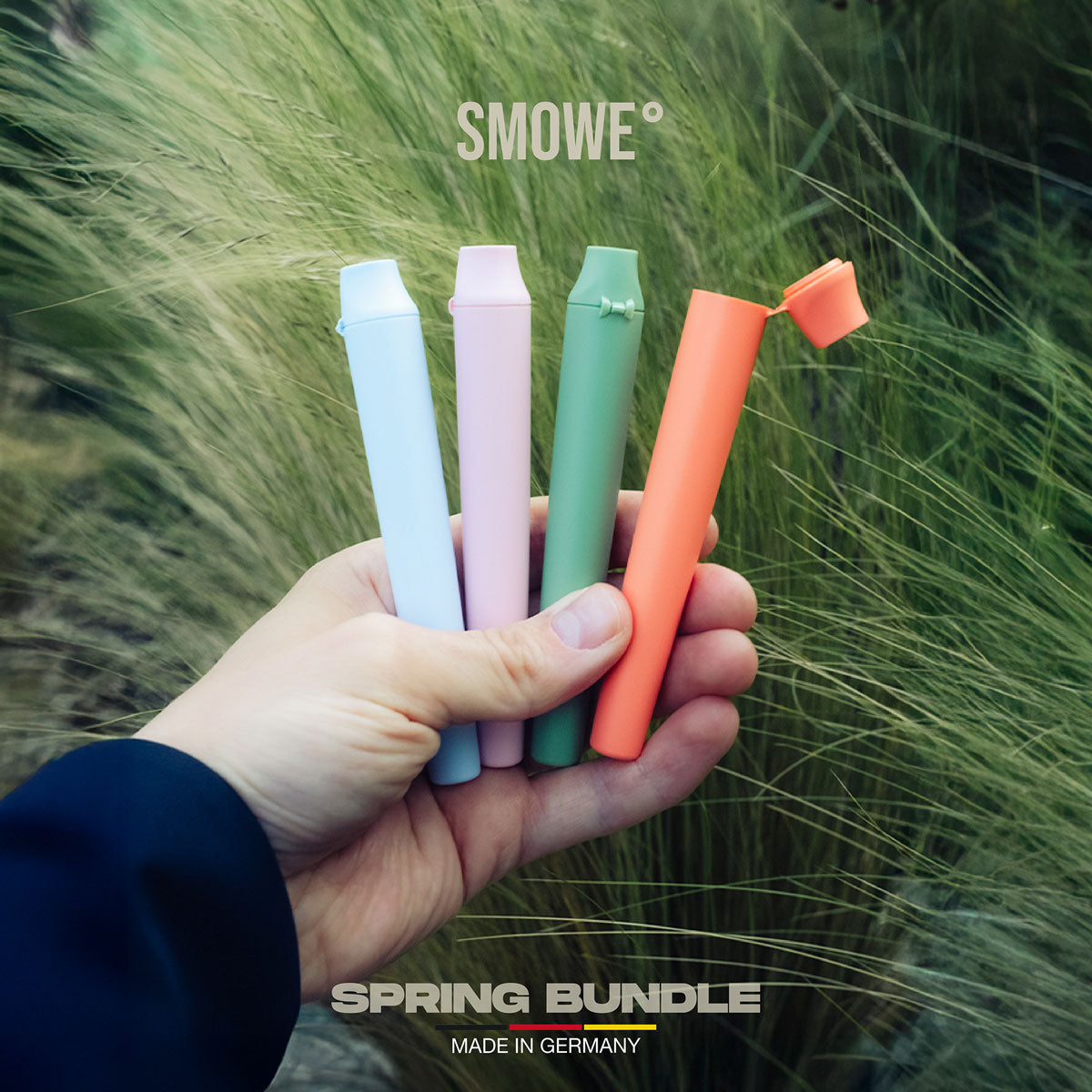 Hand hält das SMOWE Spring Bundle mit vier farbigen GREENTUBE Joint Tubes vor grünem Grashintergrund.