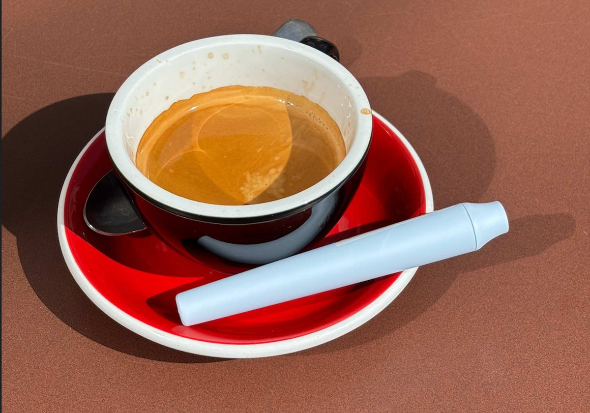 Hellblaue SMOWE GREENPOCKET geruchsdichte Transportbox für Kräuter auf roter Untertasse neben Tasse Kaffee.