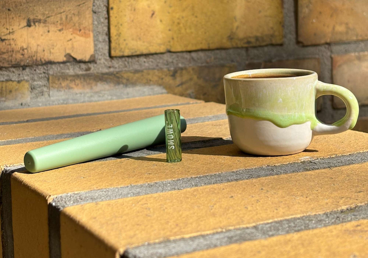 Grüne SMOWE Joint-Tube und passender Glastip-Glasfilter für Cannabis neben einer Tasse Espresso.